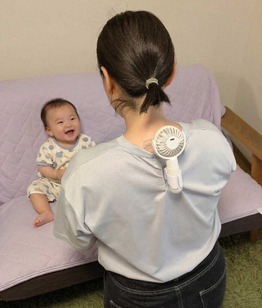 シャツの背中側にベビーカー扇風機を取り付けたお母さんが子供を抱っこしようとして近づいた様子